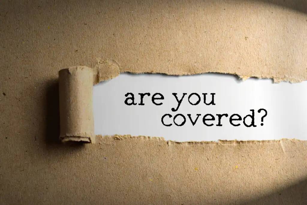 A piece of brown paper is torn back to reveal the words are you covered? printed in black text on a white background underneath. Light highlights the exposed text area.