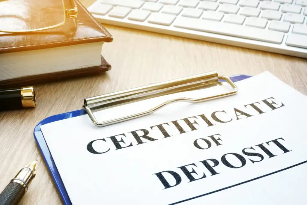 A certificate of deposit document is clipped on a blue clipboard, placed on a desk next to a fountain pen, a closed notebook, and a computer keyboard.