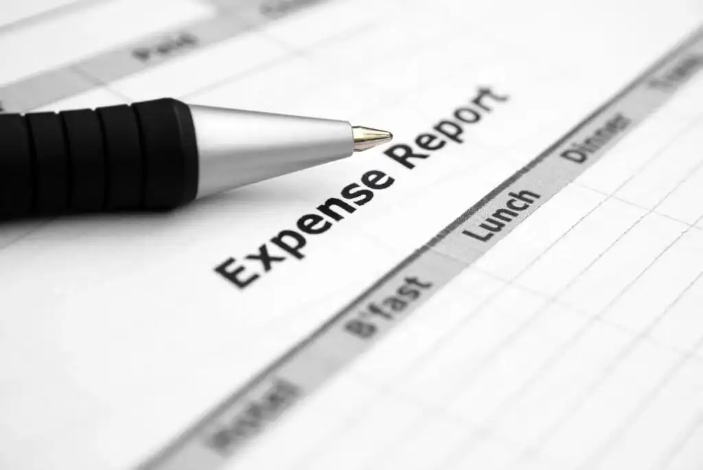 A close-up of a pen resting on a printed expense report form, showing labeled columns for Bfast, Lunch, and Dinner.
