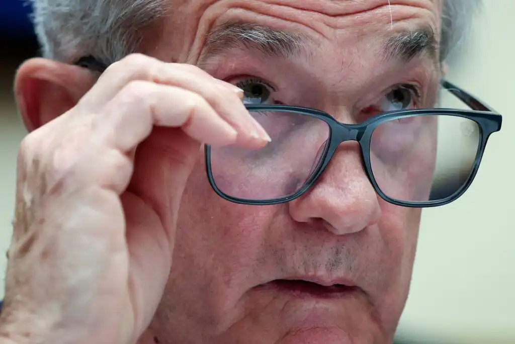 A close-up of an older man with gray hair holding his eyeglasses as he looks intently ahead, appearing thoughtful and focused.