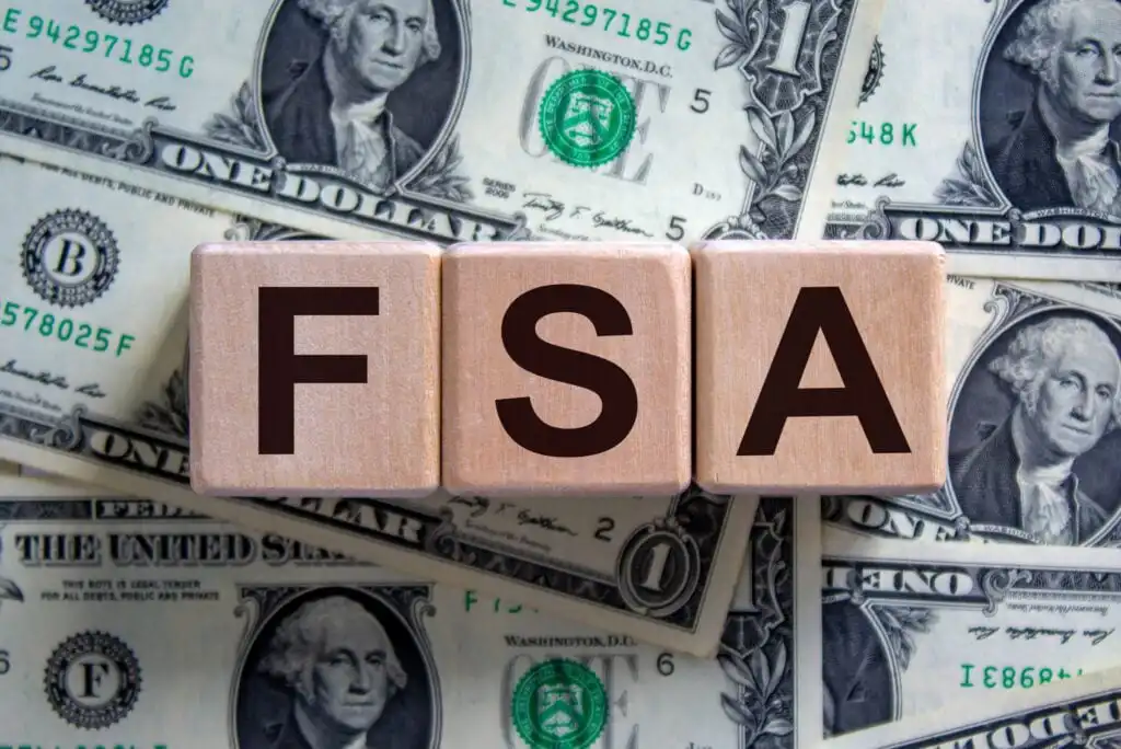 Wooden blocks spelling FSA are placed on top of several one-dollar bills, indicating a financial or savings concept.