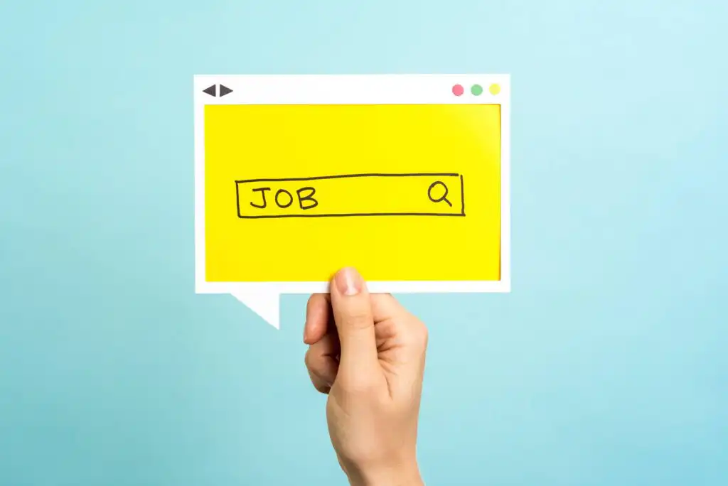 A hand holds a yellow speech bubble with a search bar illustration containing the word JOB and a magnifying glass icon, against a light blue background.