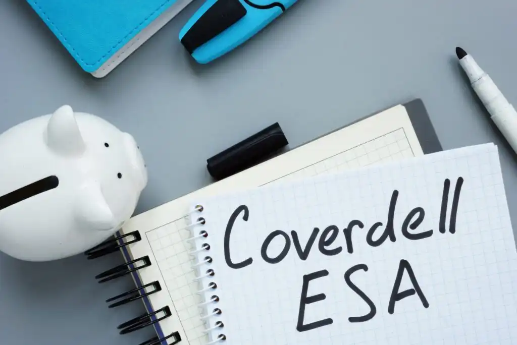 A notepad with Coverdell ESA written on graph paper, surrounded by a white piggy bank, a blue notebook, a black marker, and a blue highlighter on a gray desk.