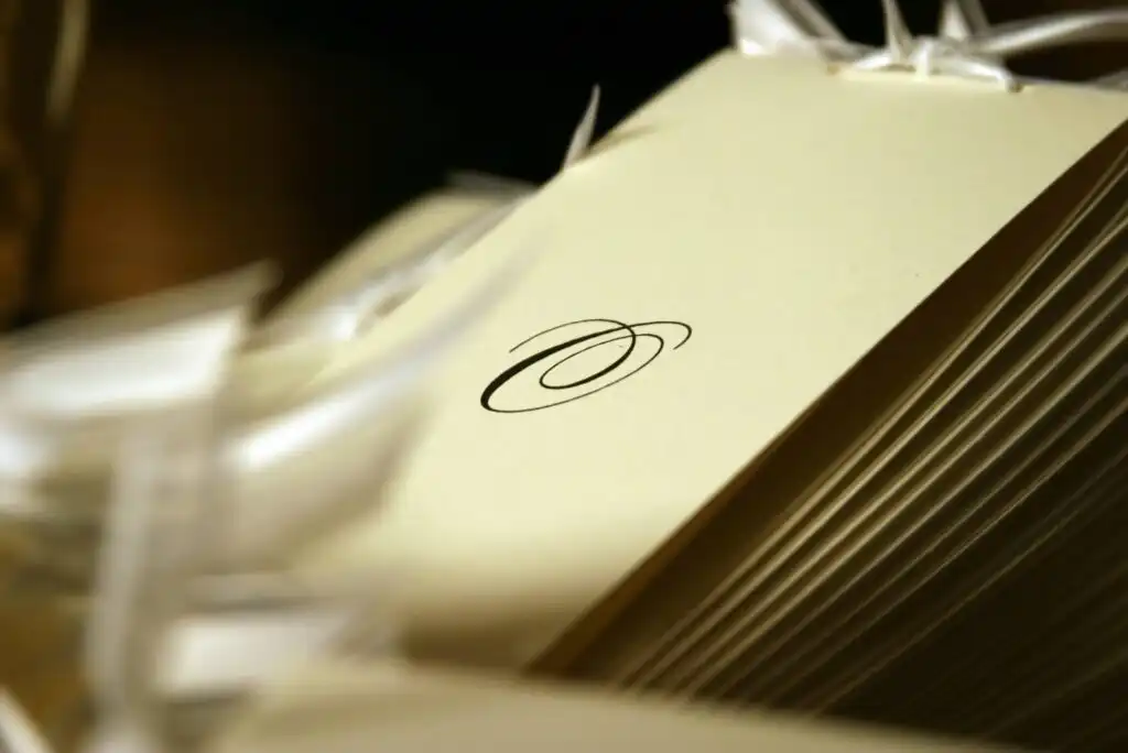 A close-up of stacked cream-colored envelopes, each adorned with an elegant black swirl design, with some white ribbon strands visible in the foreground and background.