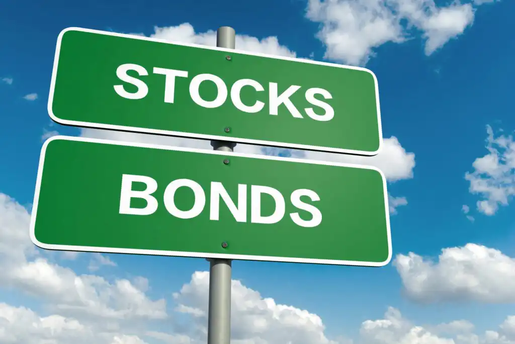 Two green road signs read STOCKS and BONDS against a blue sky with scattered clouds.